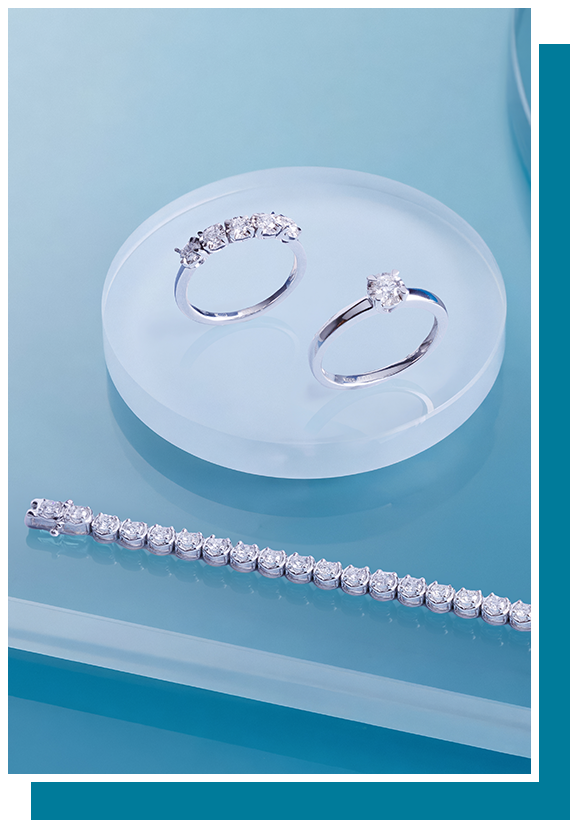 Silver diamond rings and a tennis bracelet displayed on a translucent round stand